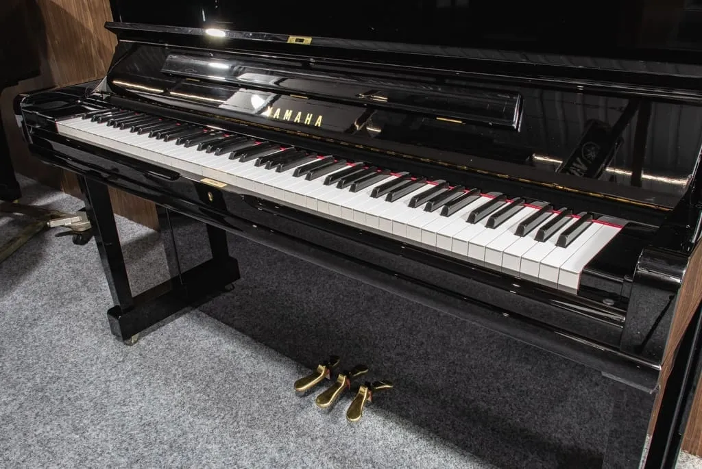 Black Yamaha YUS3 upright piano from 2008 with polished finish and three brass pedals on gray carpet.