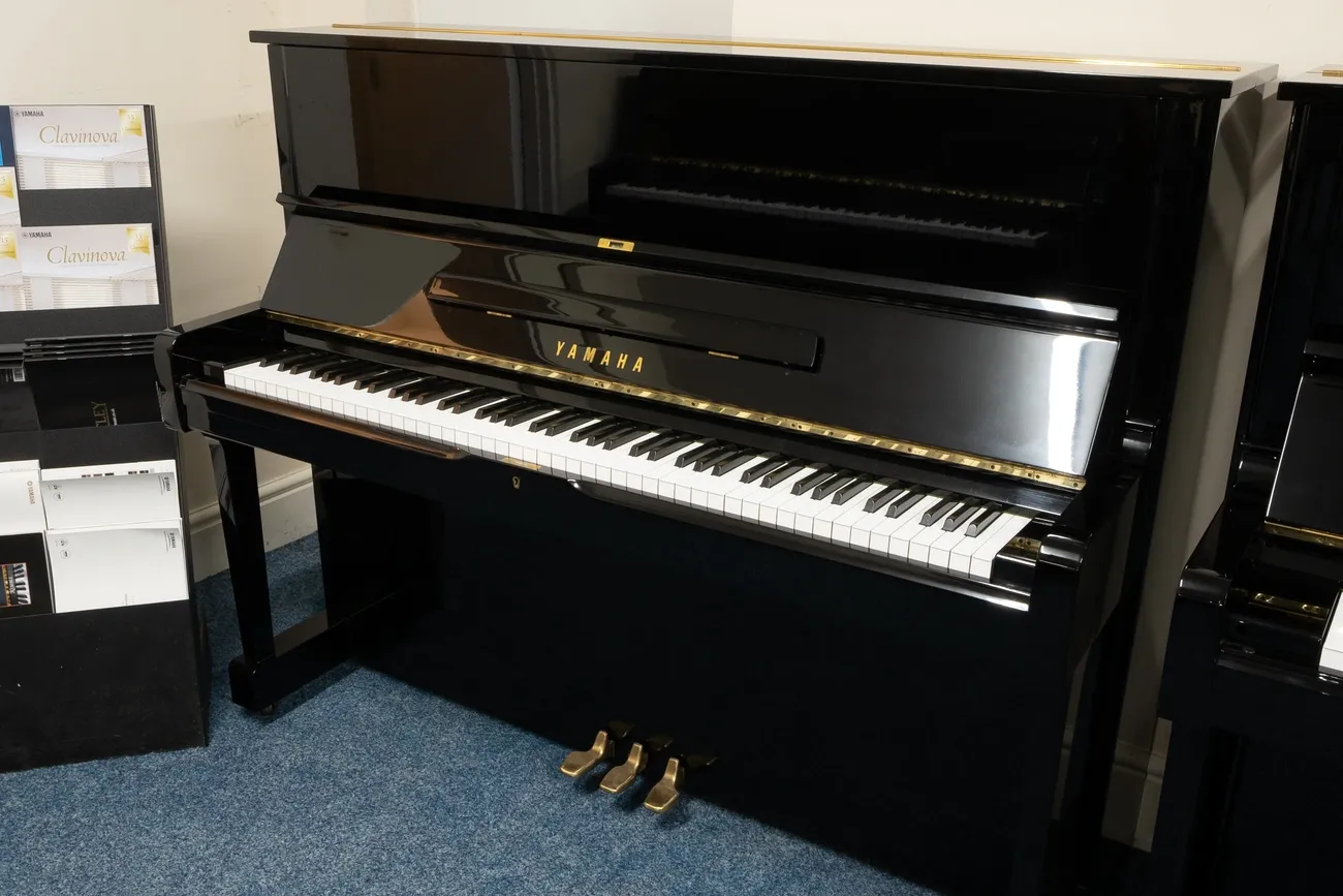 Glossy black Yamaha U1 upright piano with three pedals on blue carpet in a showroom setting
